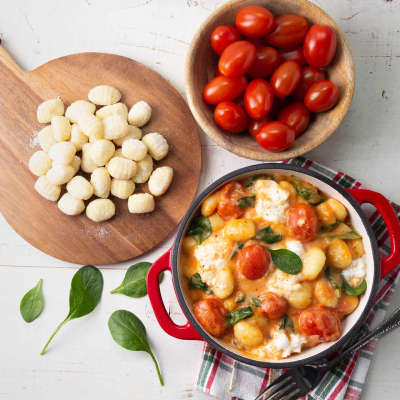 Gnocchi z pomidorkami koktajlowymi, świeżym szpinakiem i roztopioną mozzarellą na talerzu