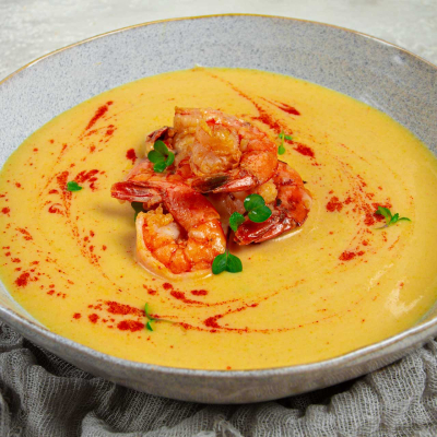 Kremowa zupa dyniowa z krewetkami, podana w misce, udekorowana świeżymi ziołami