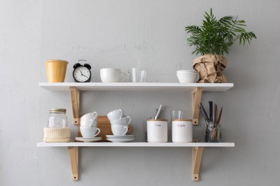 Porcelanowe kubki na półce w kuchni obok kwiatka, słoika i zegarka
