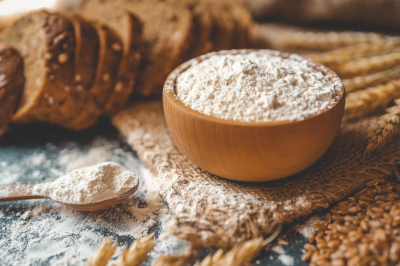 Mąka w miseczce, łyżka i kromki chleba na stole kuchennym